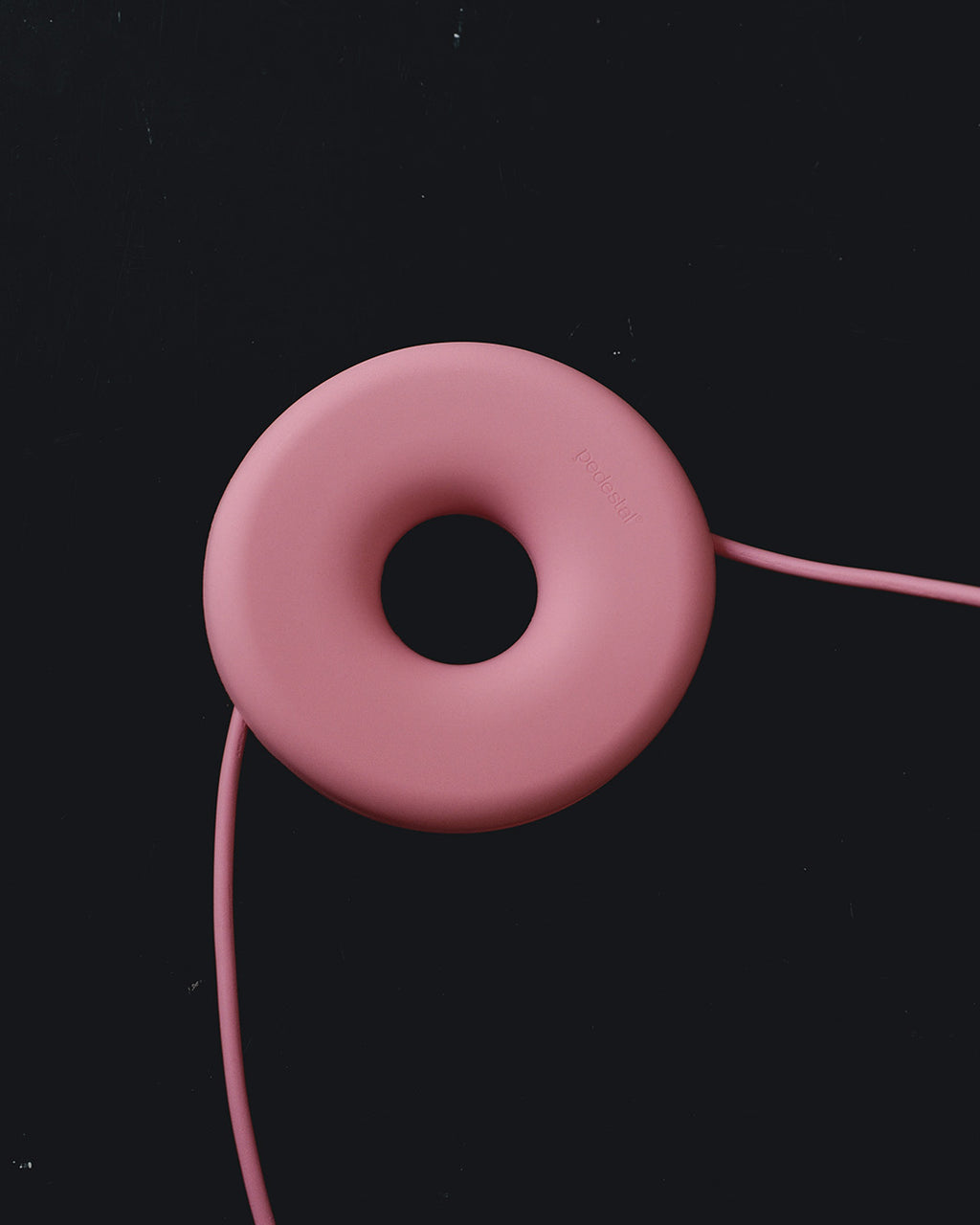 Bubble Gum pink Cable Bagel cable manager on black studio backdrop, matte donut form with cord routed through it