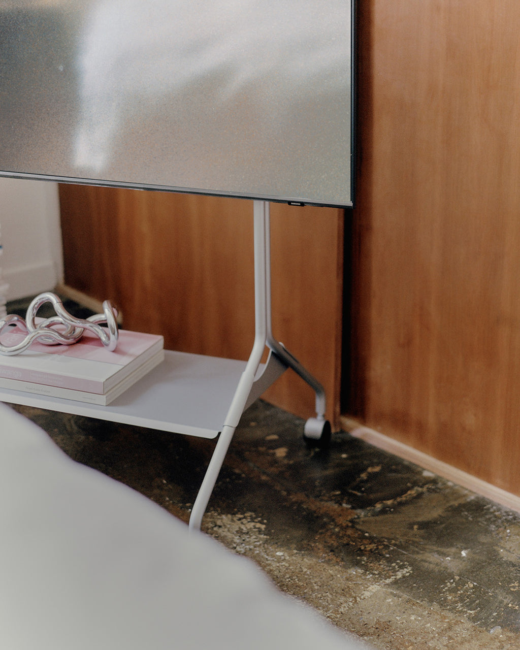 Moon in Cloudy Silver TV stand with wheels in a wood-paneled room, close-up of shelf holding books and decor