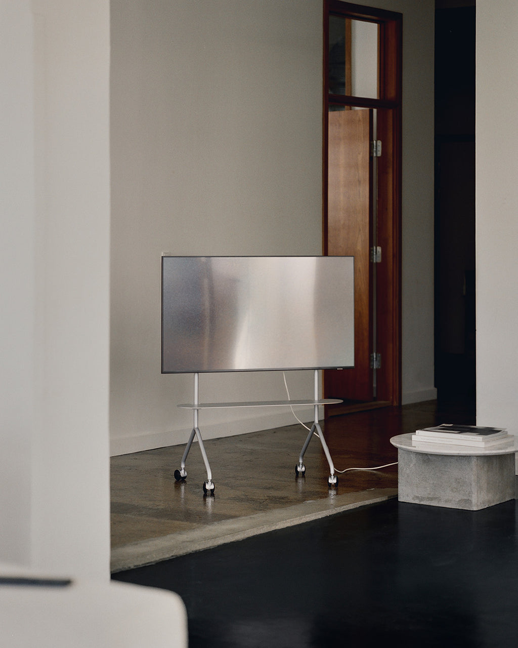 Moon Light in Cloudy Silver rolling TV stand with wheels holding a flat screen in a minimal concrete-floor living room