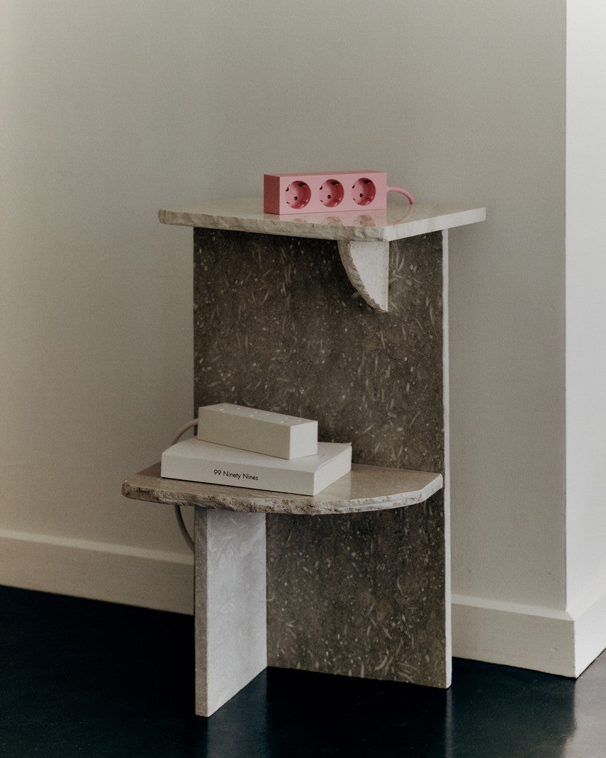 Power Bar in Pearl resting on a book atop a stone side table, with a pink power bar on the shelf above